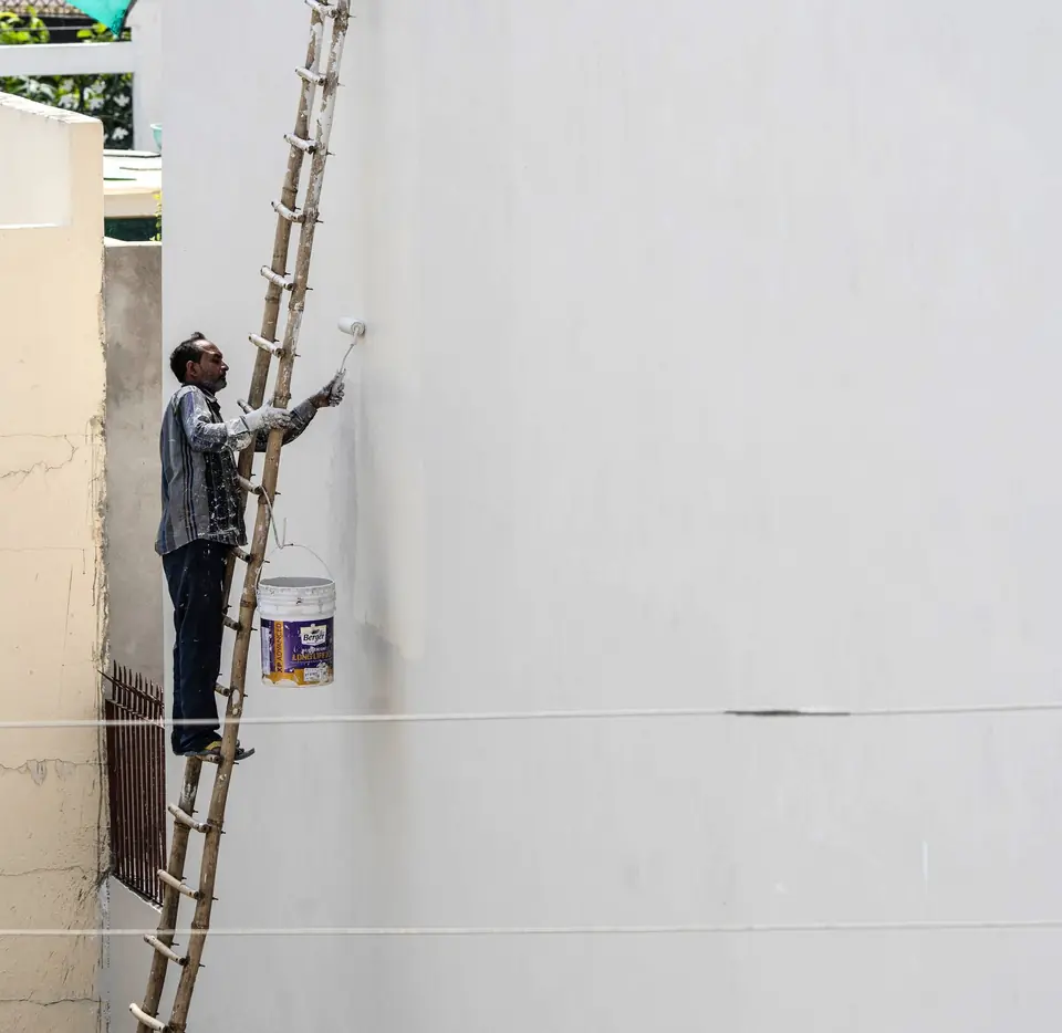 Peintre appliquant une peinture de façade sur le mur extérieur d'une maison